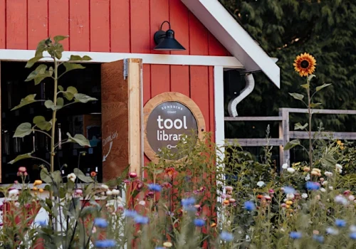 Barn with a sign saying "tool library" and lush flower beds